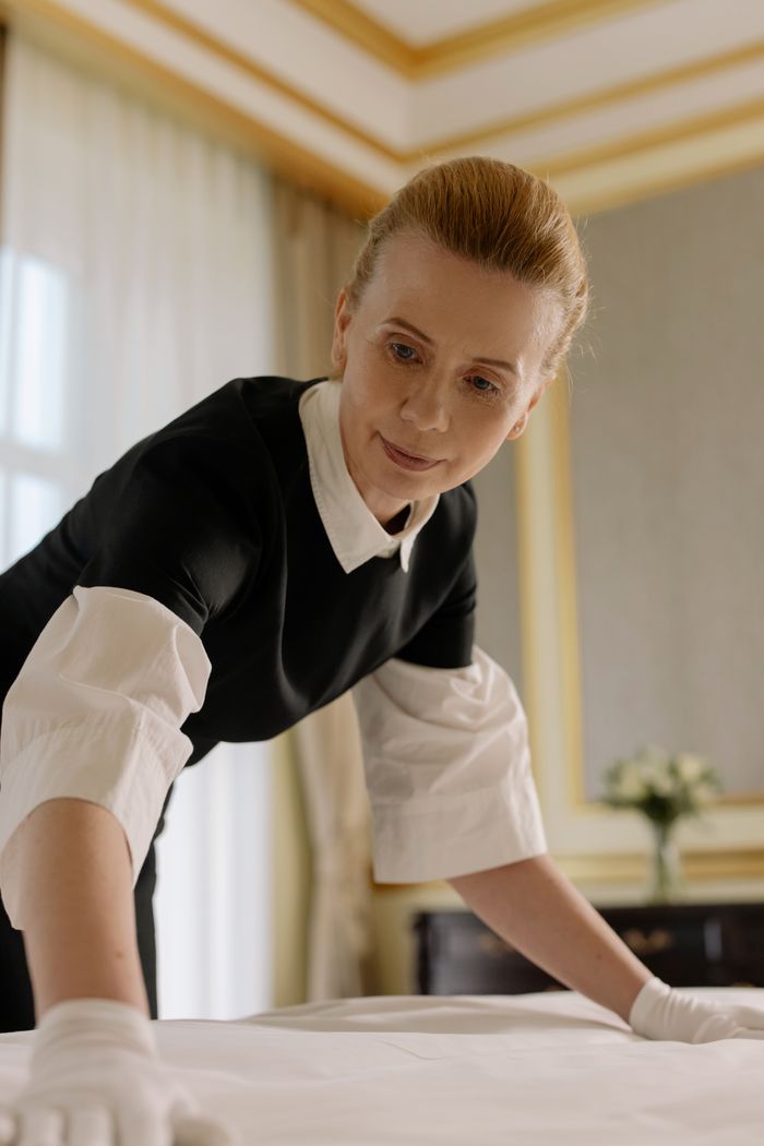 journey A housekeeper in uniform skillfully arranges bed linen in a luxurious hotel room.