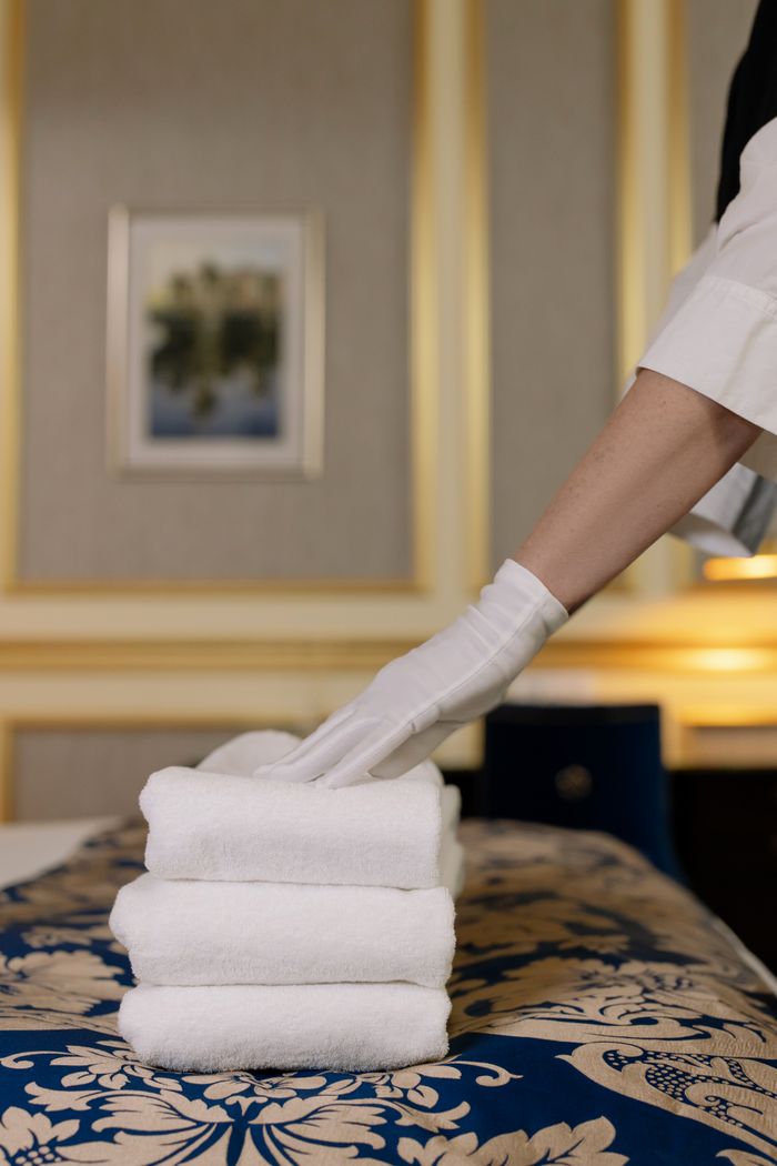 why-choose-us A hotel housekeeper in uniform arranges freshly laundered towels in a luxurious room.