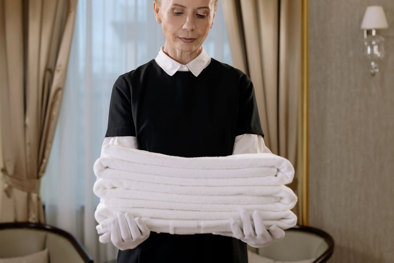 team-01 Professional housekeeper holding a stack of fresh towels in a luxurious hotel room, showcasing elegance and service.