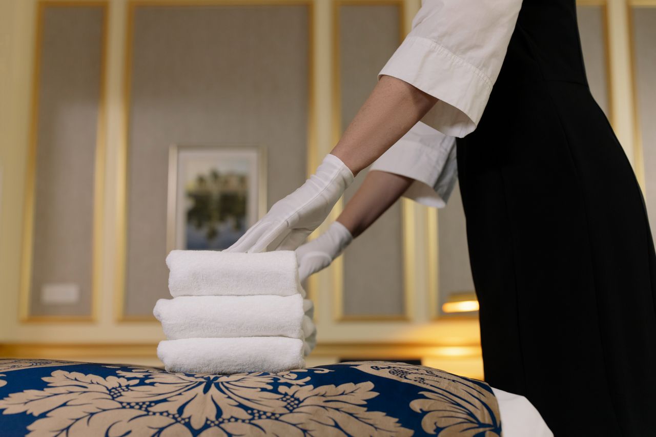 services-03 A hotel housekeeper neatly stacks fresh towels in a luxurious room setting.
