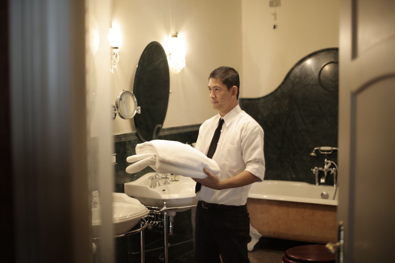 services-02 Side view of young male employee holding stack of white towels while standing in bathroom of luxury hotel